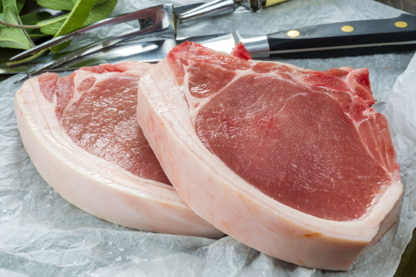 raw pork chops with carving knife and fork