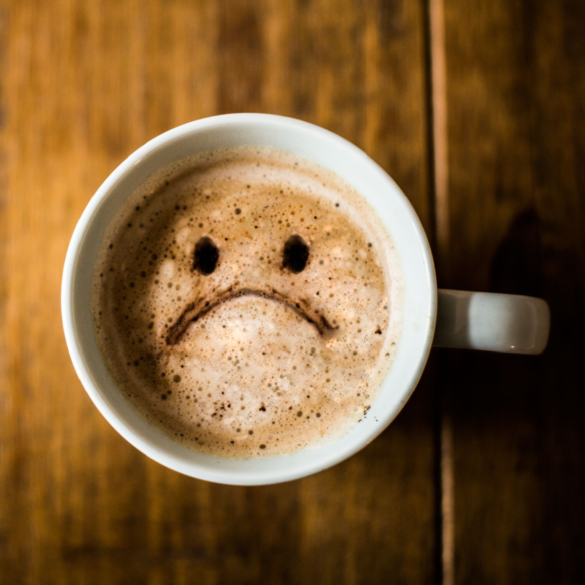 sad unhappy face on coffee foam wooden background