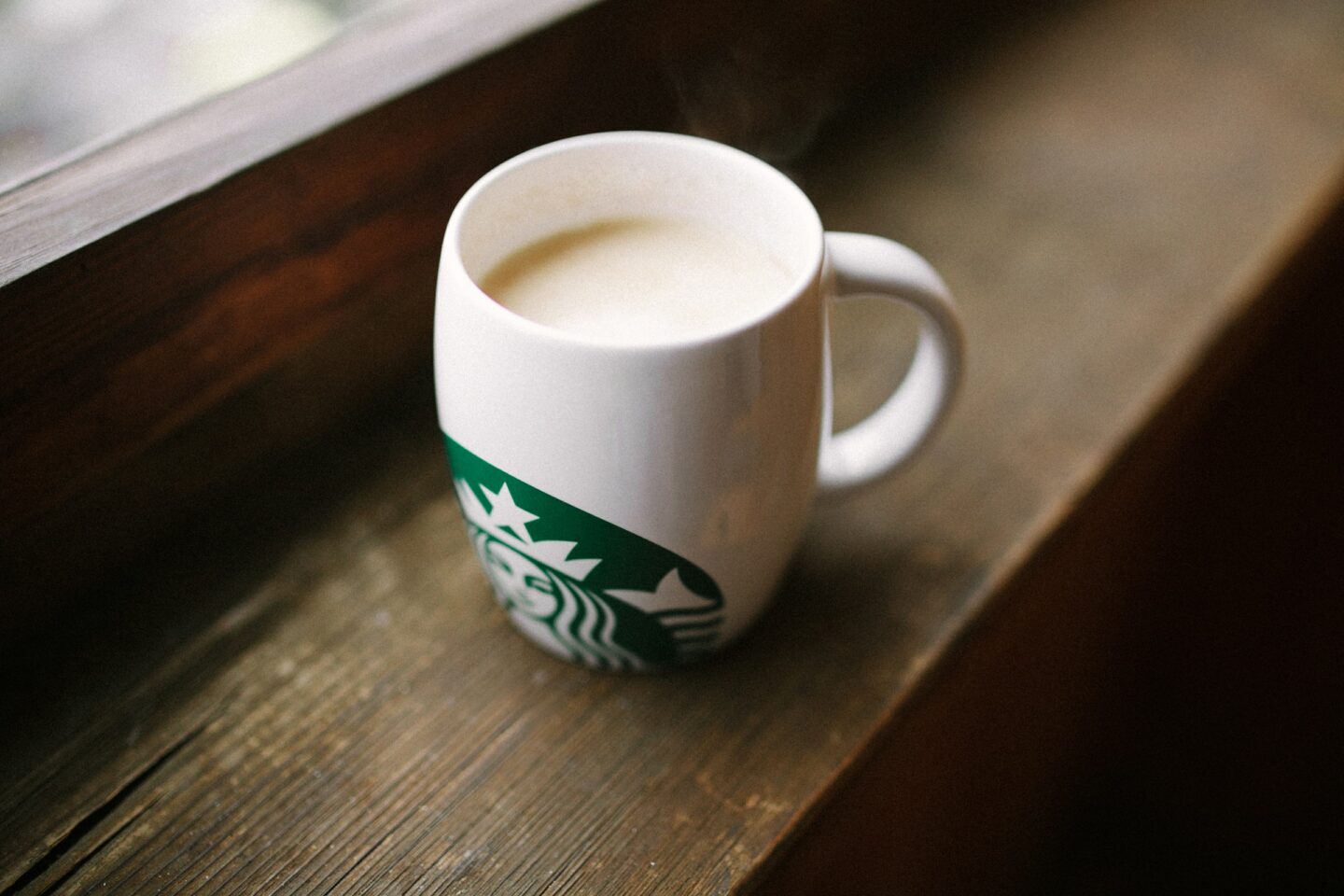 starbucks ceramic mug containing coffee on wooden windowsill