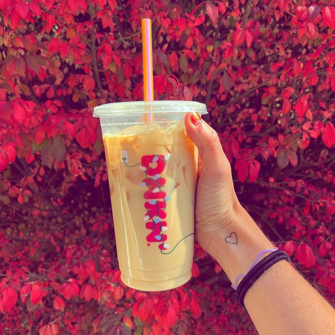 tattooed hand holding up cup of dunkin donuts iced coffee red leaves in background