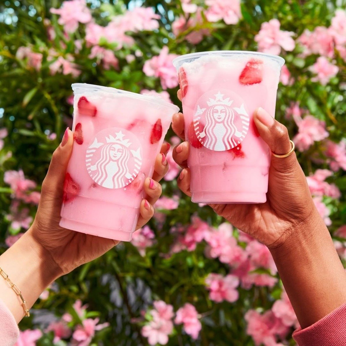 two female hands each holding up cups of starbucks pink drink