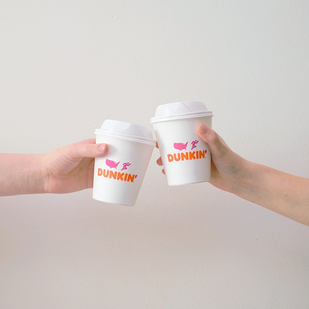 two people holding dunkin donuts paper cups together