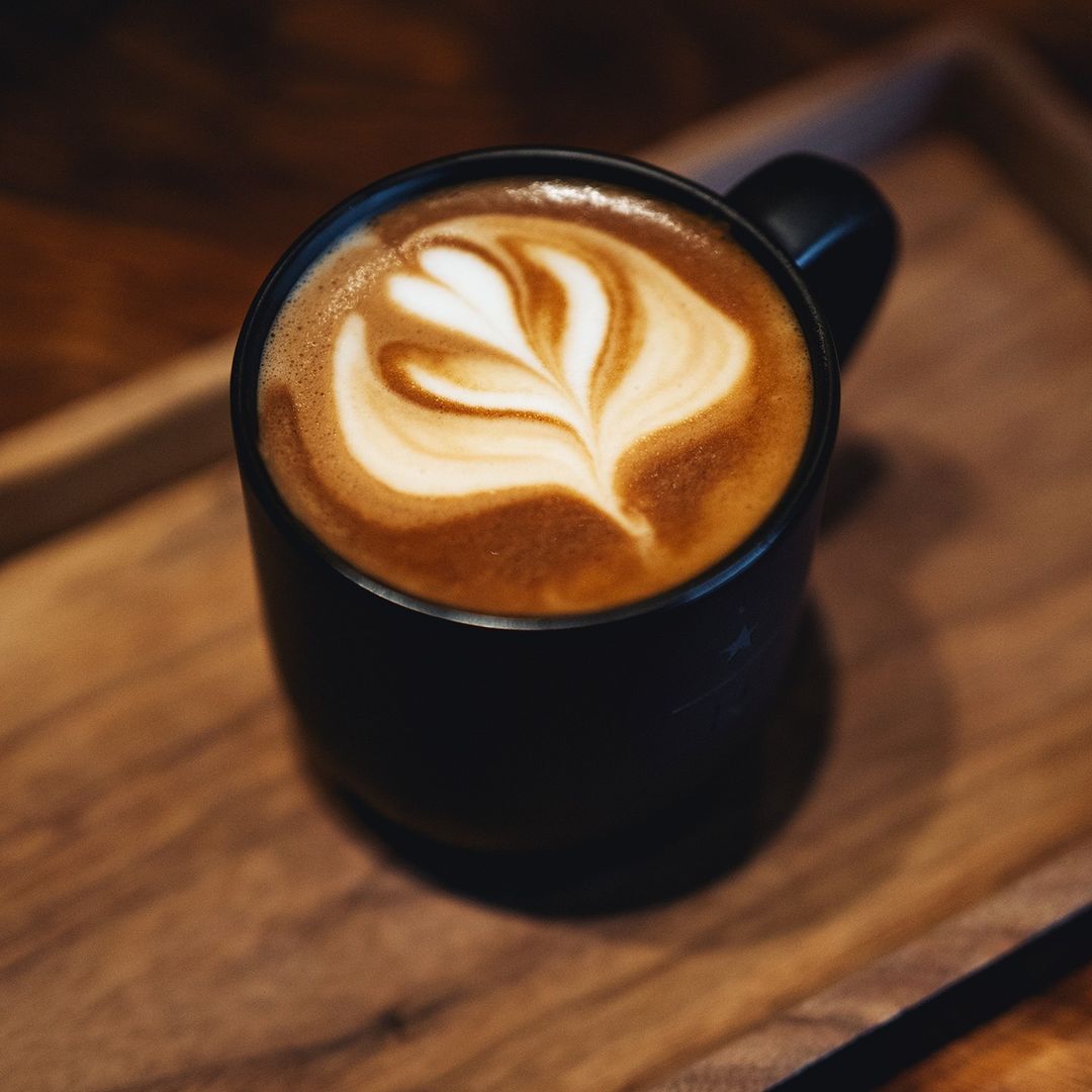 warm latte in black starbucks ceramic mug on wooden tray