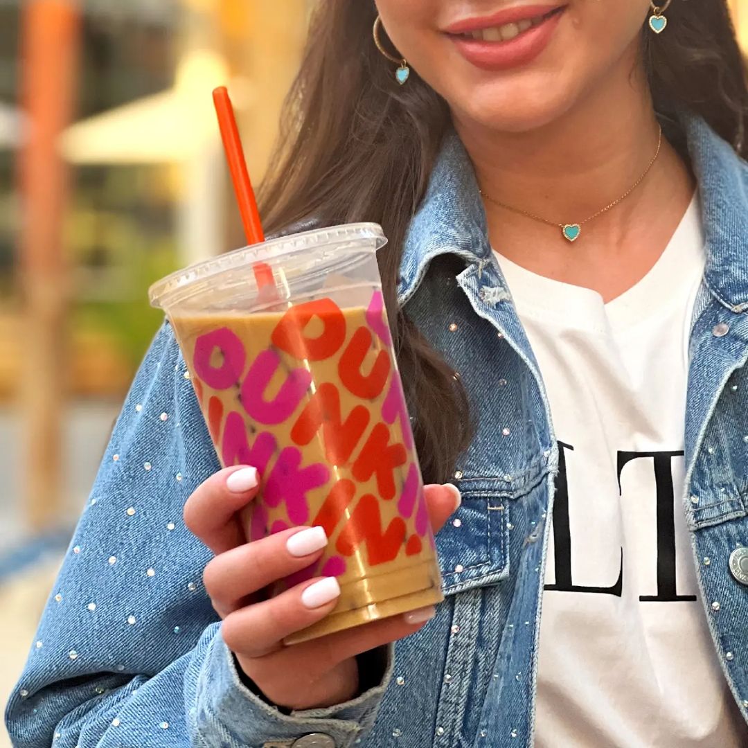 woman smiling while showing cup of dunkin donuts iced coffee
