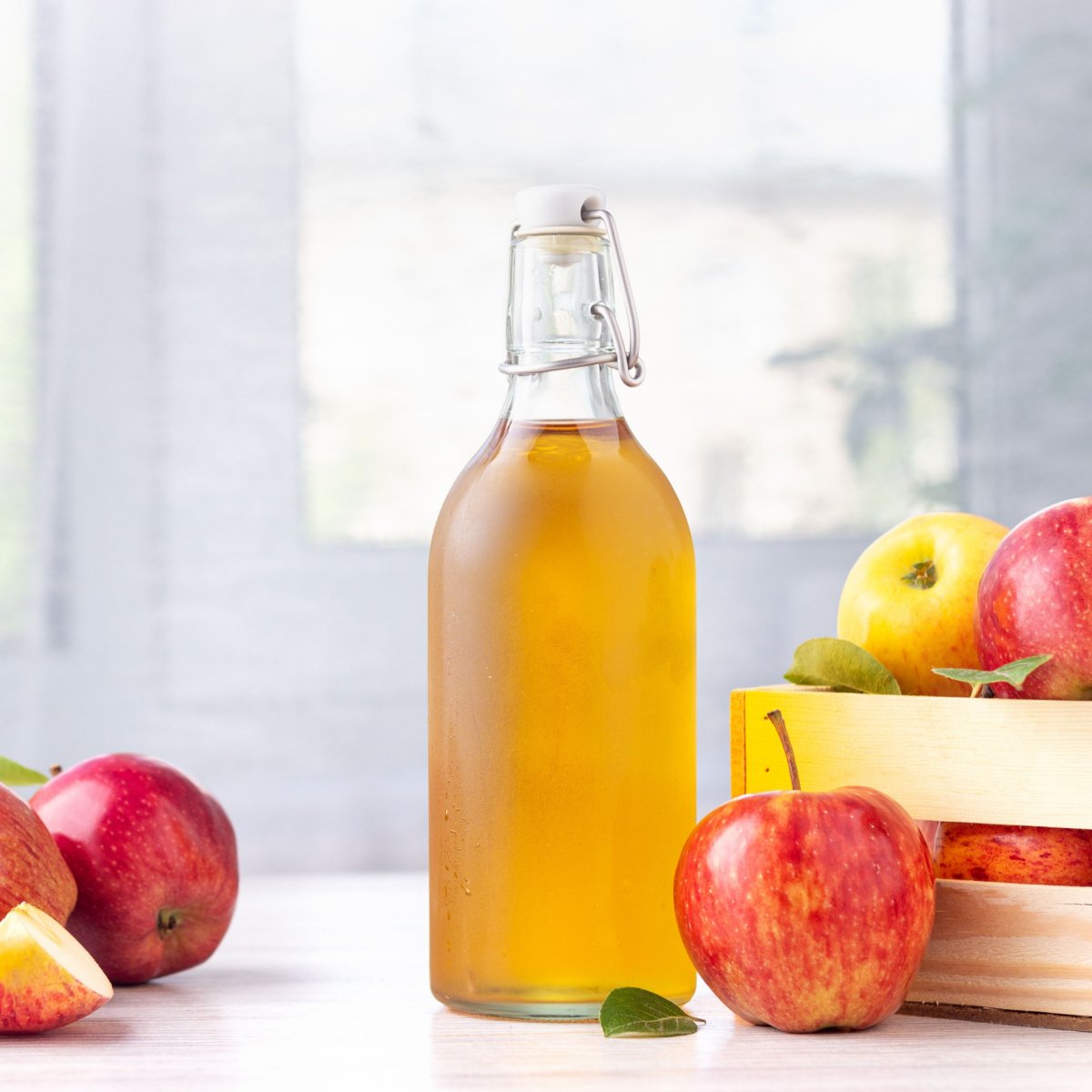 apple cider vinegar in glass bottle on white table beside box of fresh ripe apples