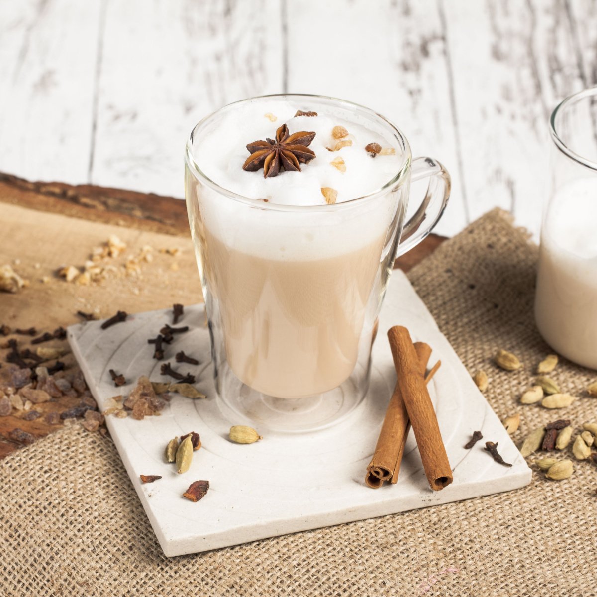 chai tea latte in glass mug on white saucer with spices spread around (1)