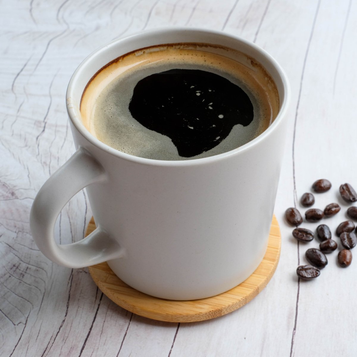 cup of freshly made americano in white ceramic mug on wooden saucer on table