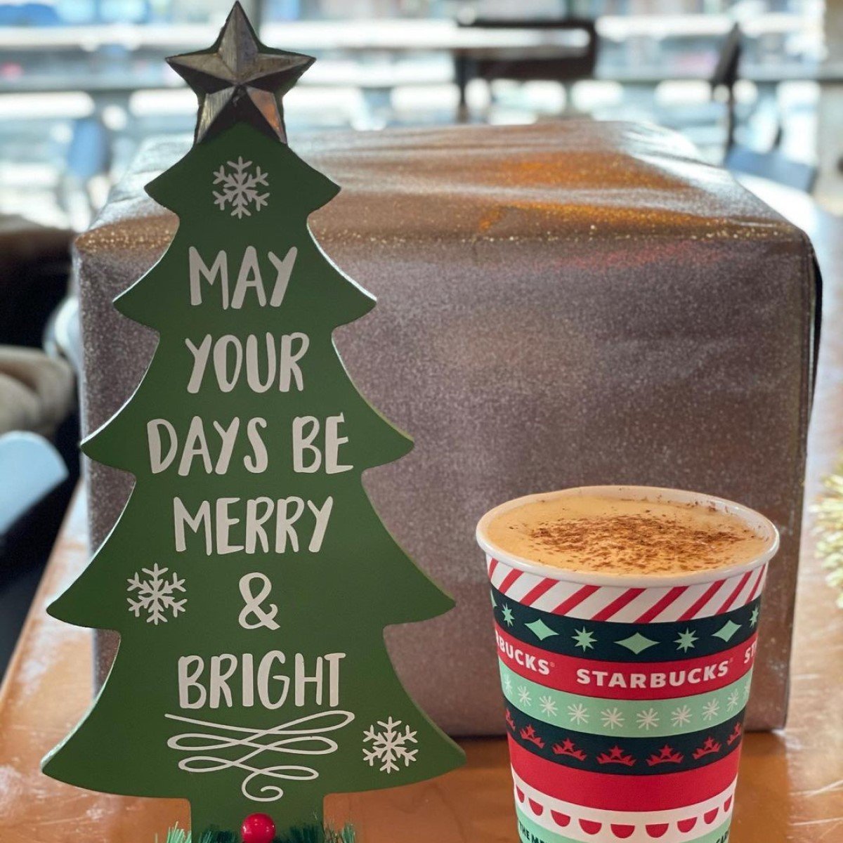 cup of hot starbucks eggnog latte on wooden table beside small tree with words on it