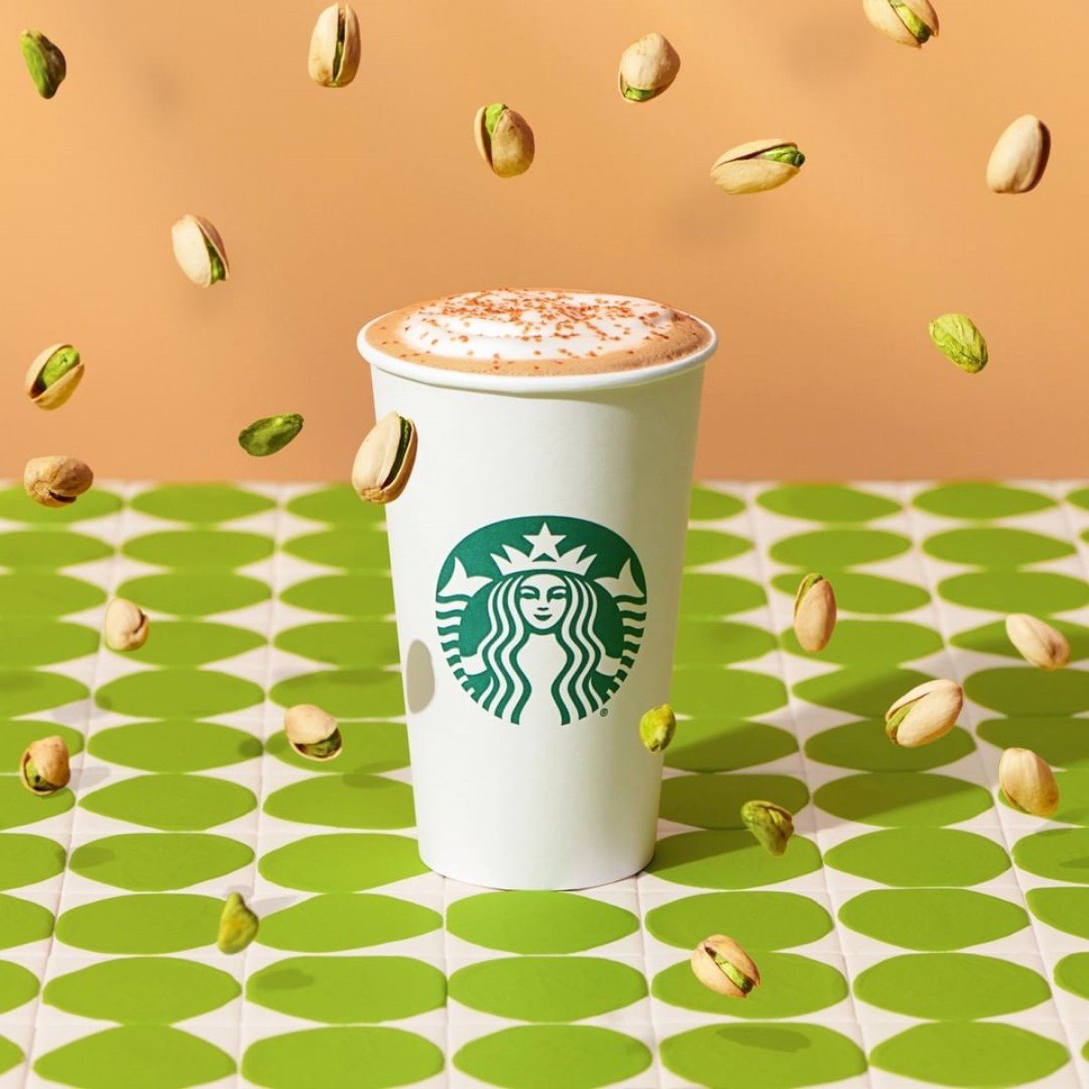 cup of hot starbucks pistachio latte on green white table with pistachios raining down
