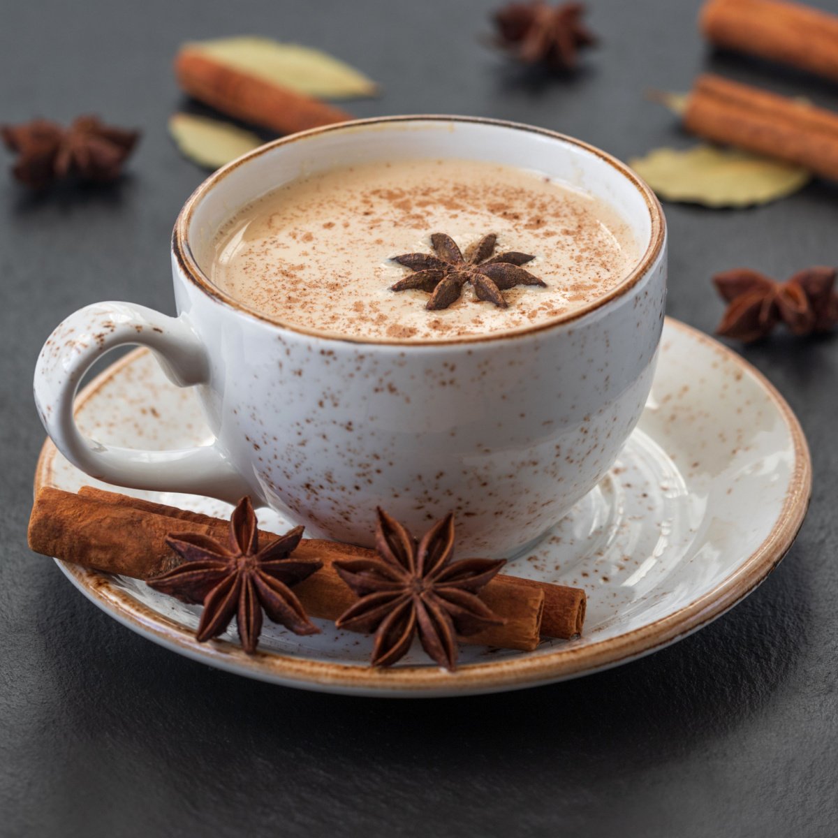 cup of indian masala chai tea on saucer with various spices scattered on table