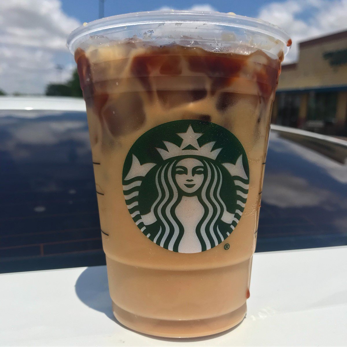 cup of starbucks iced dirty chai tea latte on white surface with car in background
