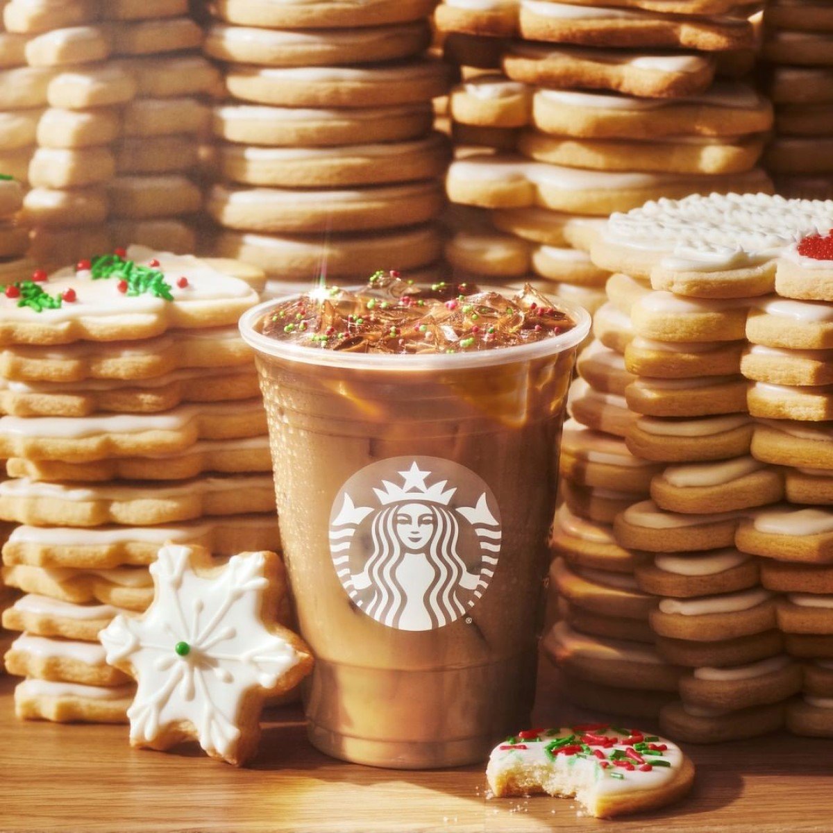 cup of starbucks iced sugar cookie almond milk latte on wooden table with stacks of sugar cookies