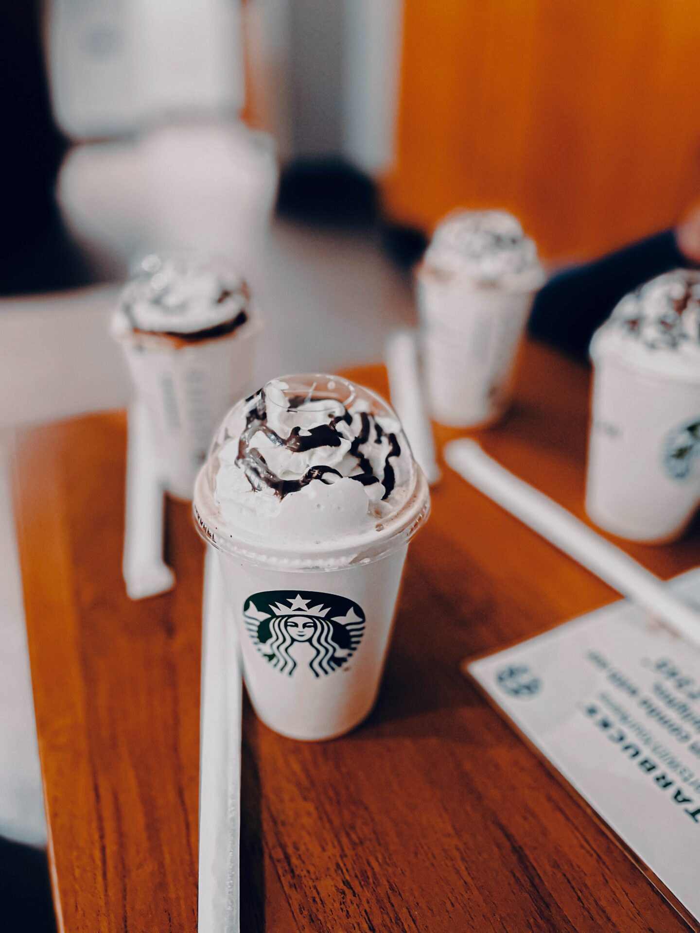 four starbucks frappuccinos in starbucks takeaway cups on wooden table