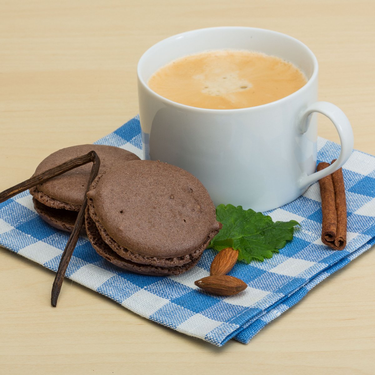french vanilla coffee in white ceramic mug beside macaroons and vanilla sticks on blue hankerchief