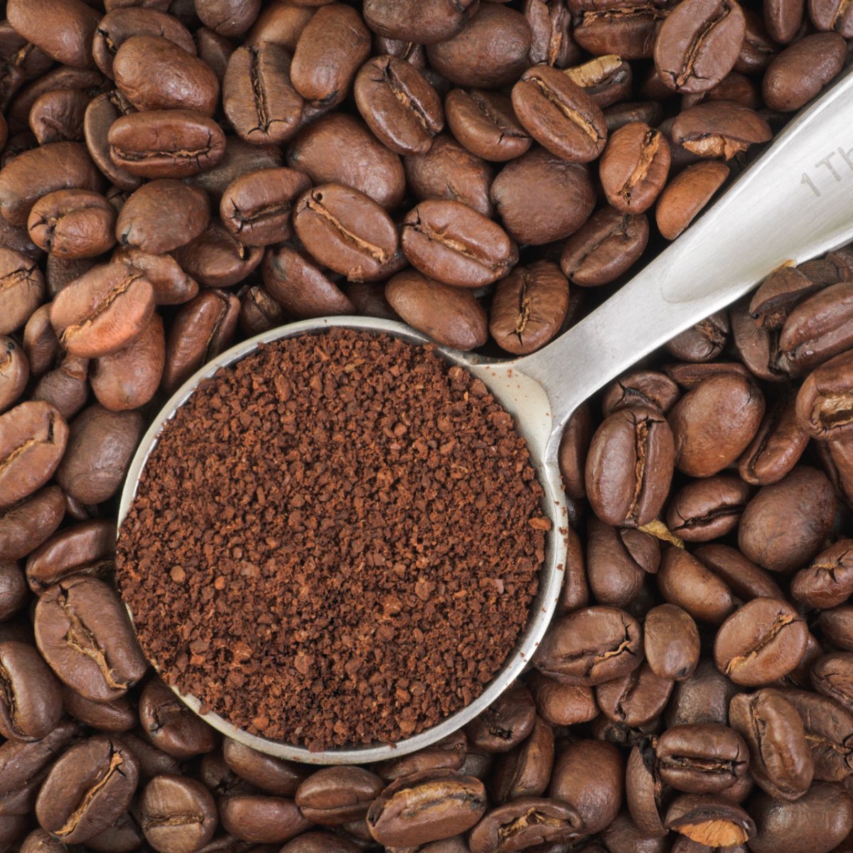 ground coffee filled tablespoon placed on top of pile of whole coffee beans