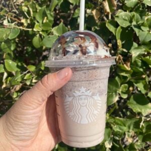 hand holding cup of starbucks cookies and cream frappuccino with leaves in background