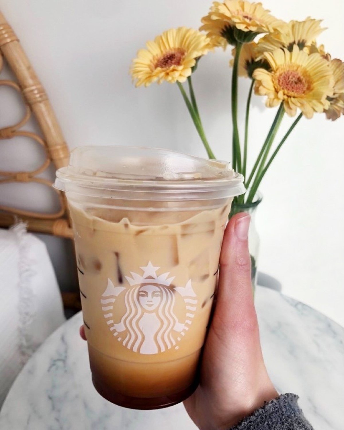 hand holding cup of starbucks iced toasted vanilla oatmilk shaken espresso in transparent cup sunflowers in background