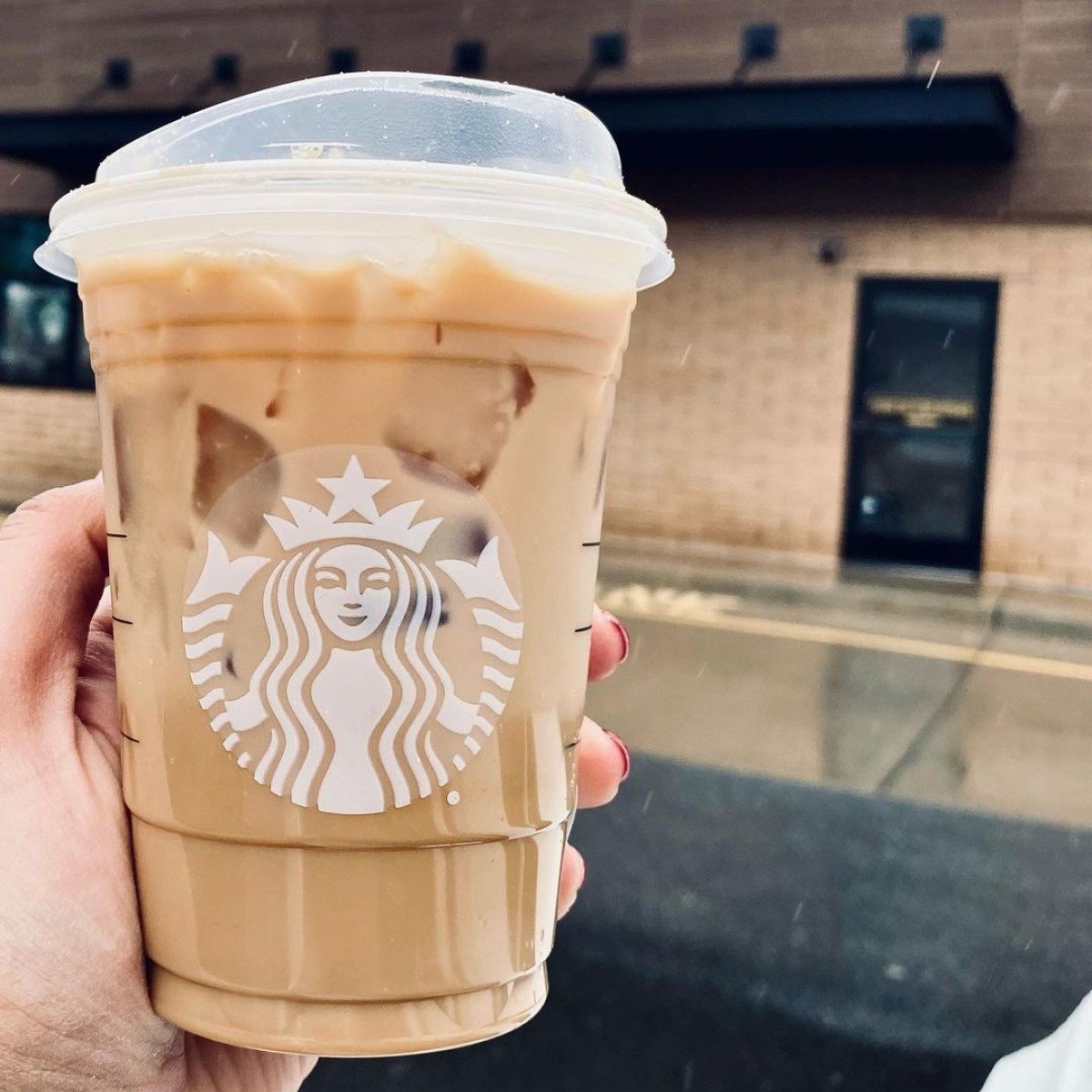 hand holding up cup of starbucks iced honey oat milk latte in transparent disposable cup