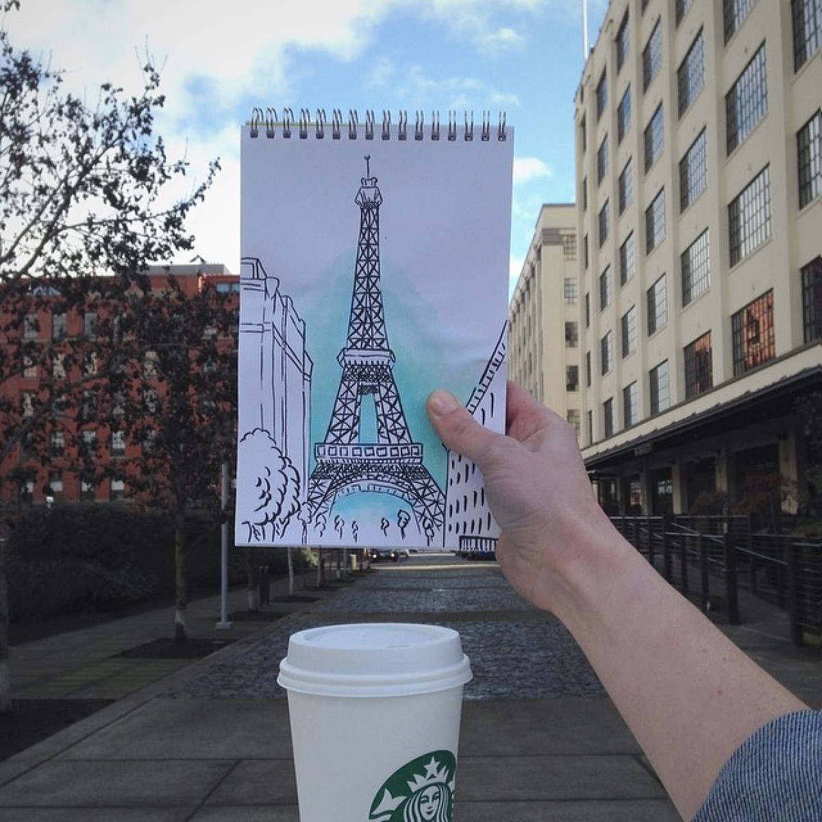 hand holding up sketch of the eiffel tower above a cup of starbucks french vanilla latte in white paper cup