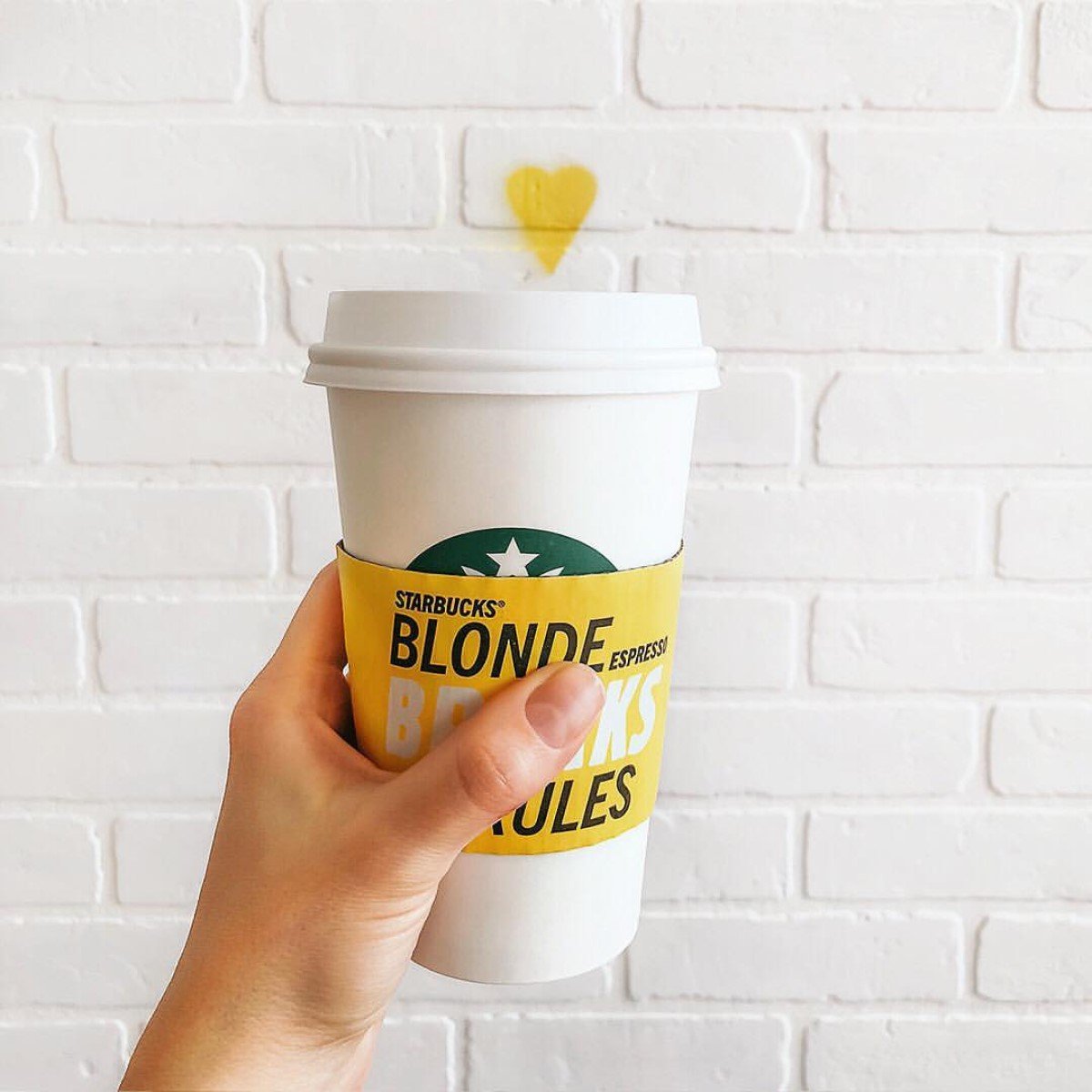 hand holding up starbucks blonde espresso in white disposable cup with yellow coffee sleeve labeled starbucks blonde espresso