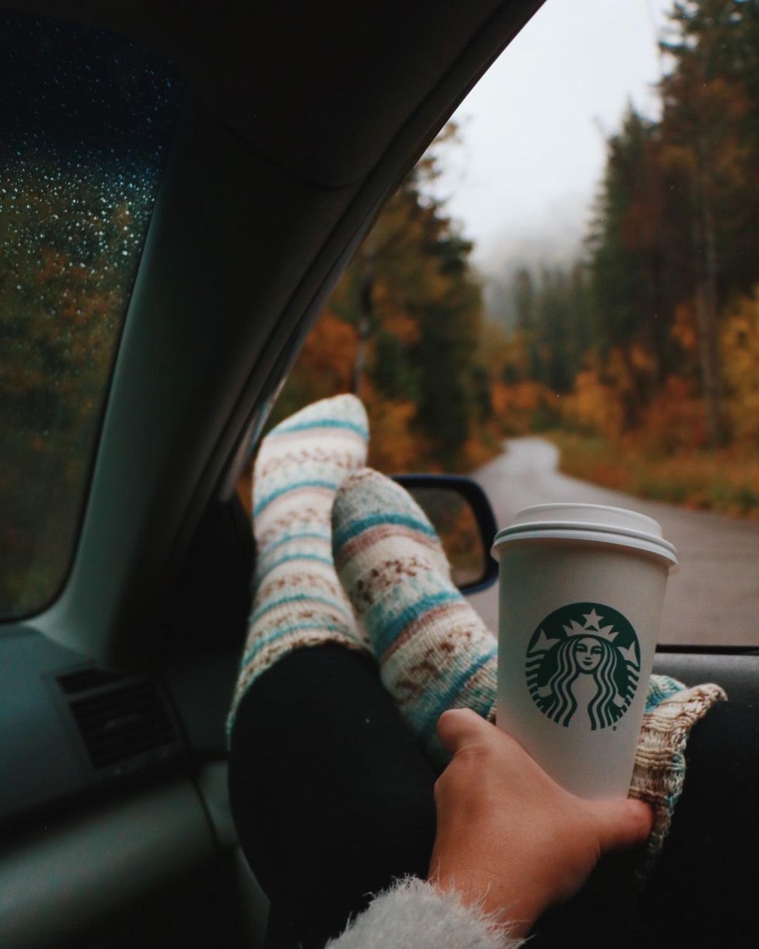 hand holding white starbucks disposable paper cup feet up on car window