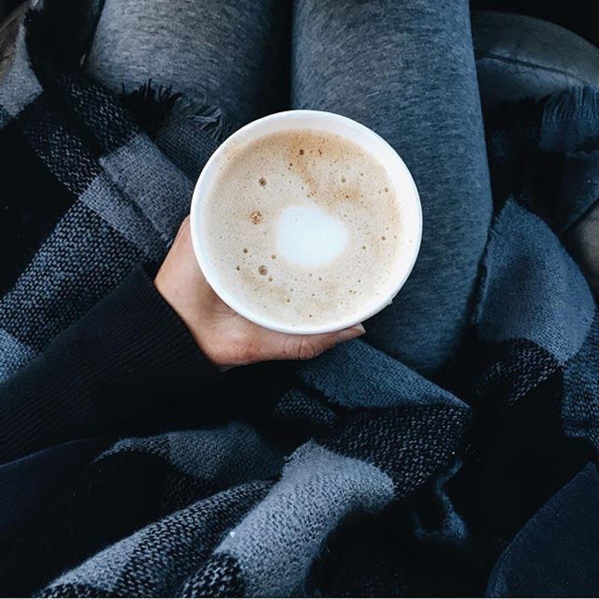 hand in black sweater holding cup of starbucks flat white in paper cup