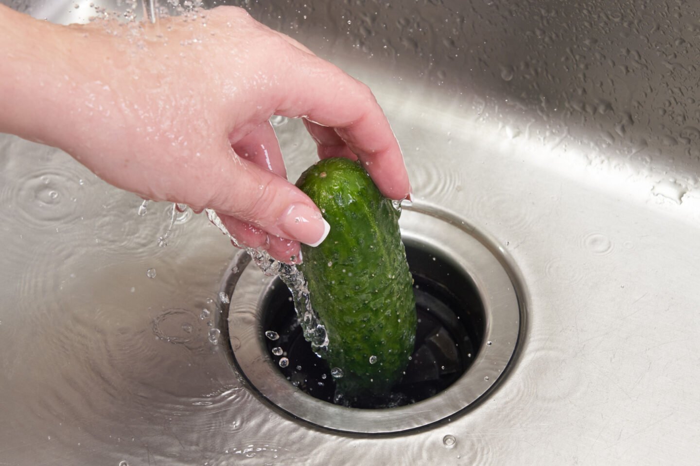 hand puts whole cucumber into grabage disposal