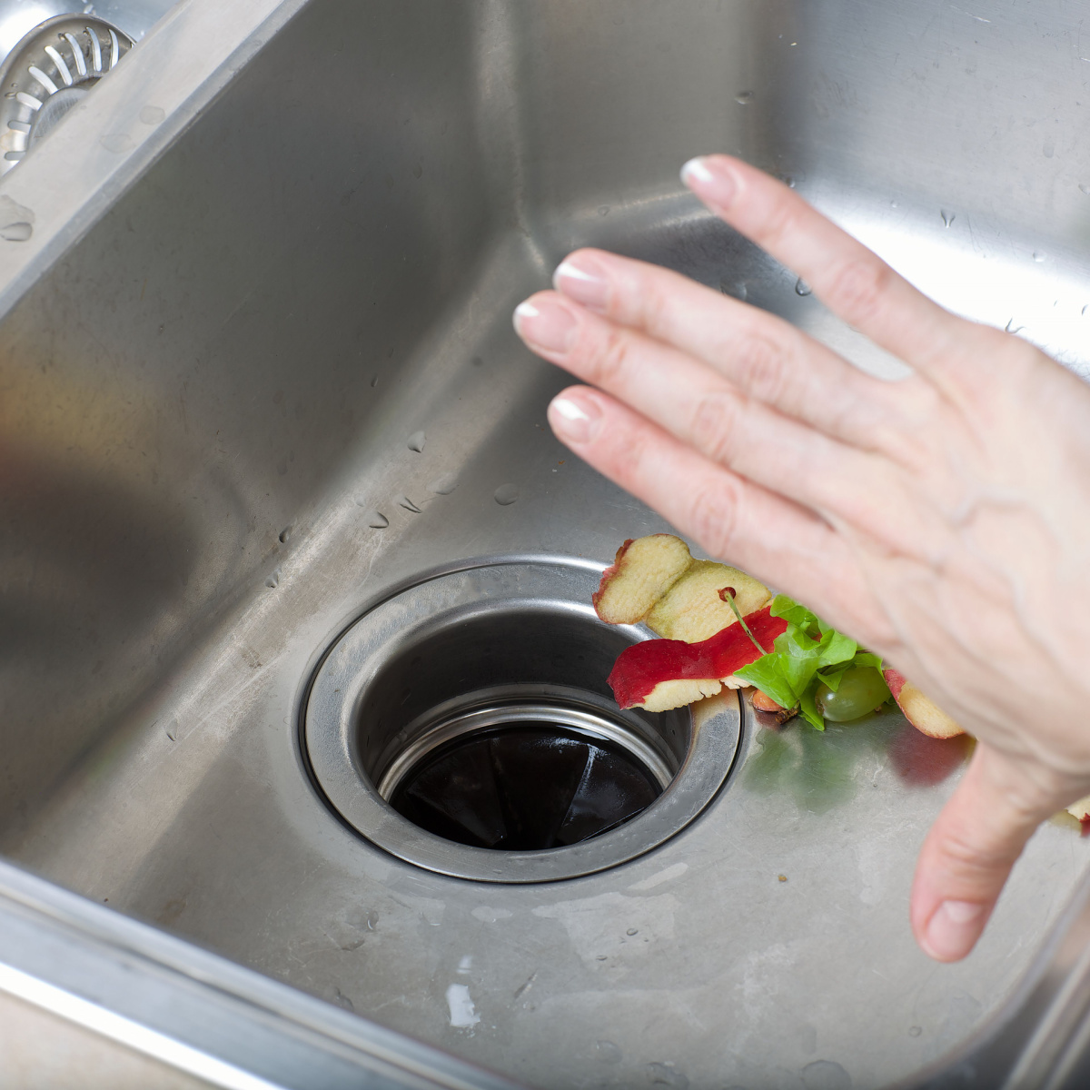 hand stopping food waste from getting into garbage disposal sink