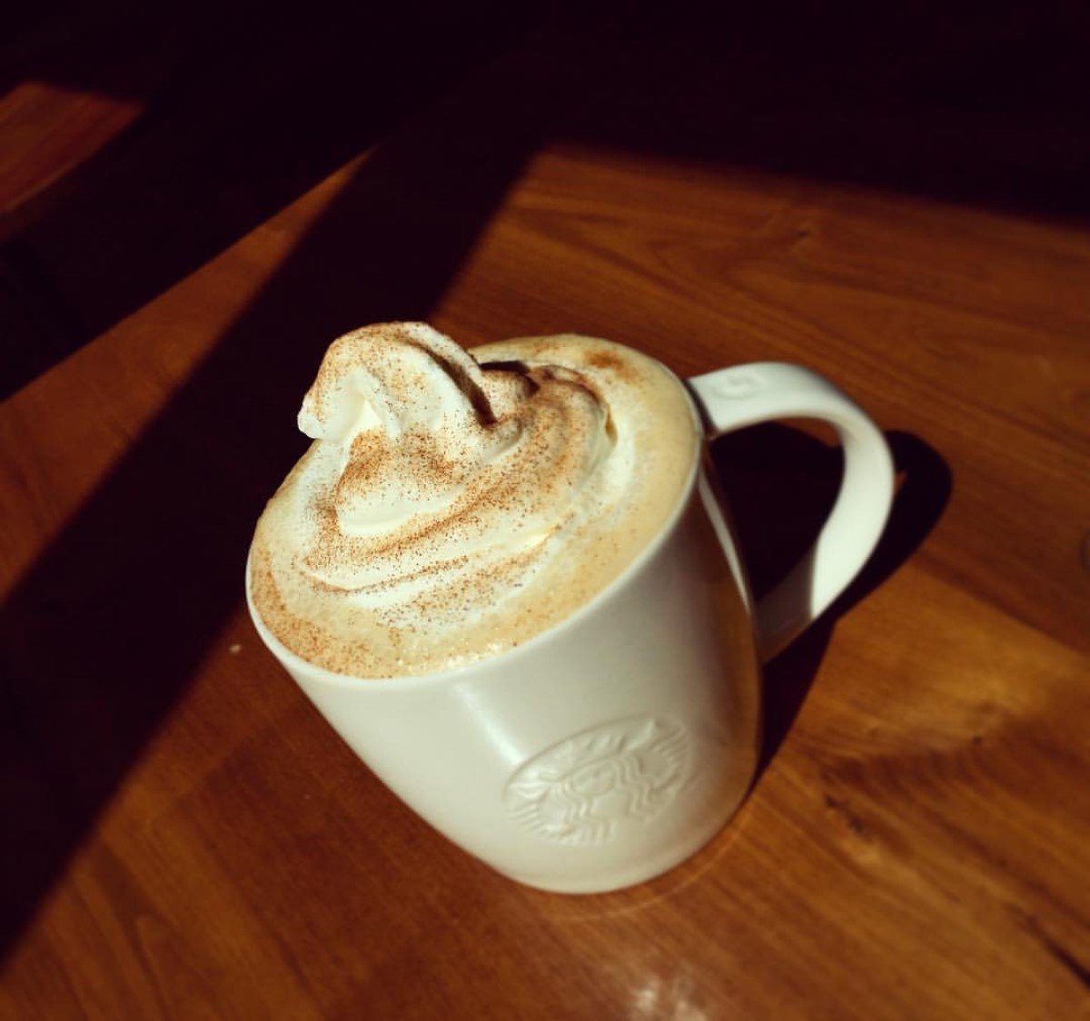 hot starbucks cinnamon dolce latte in white starbucks ceramic mug on wooden table