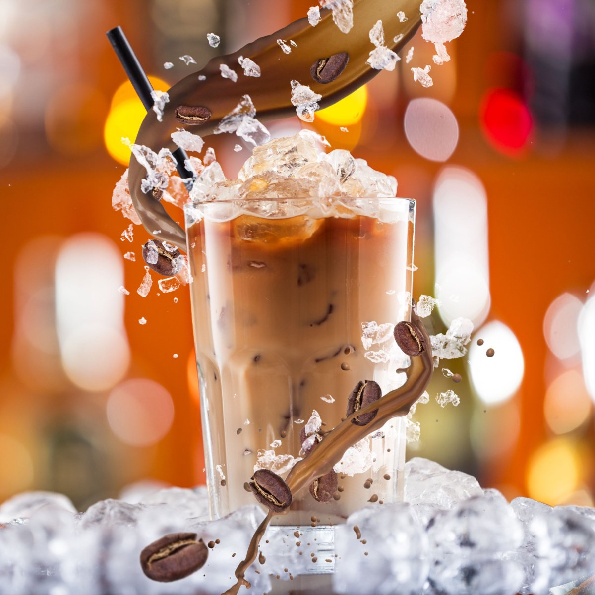 ice chips and coffee beans splashing into cold coffee in tall transparent glass