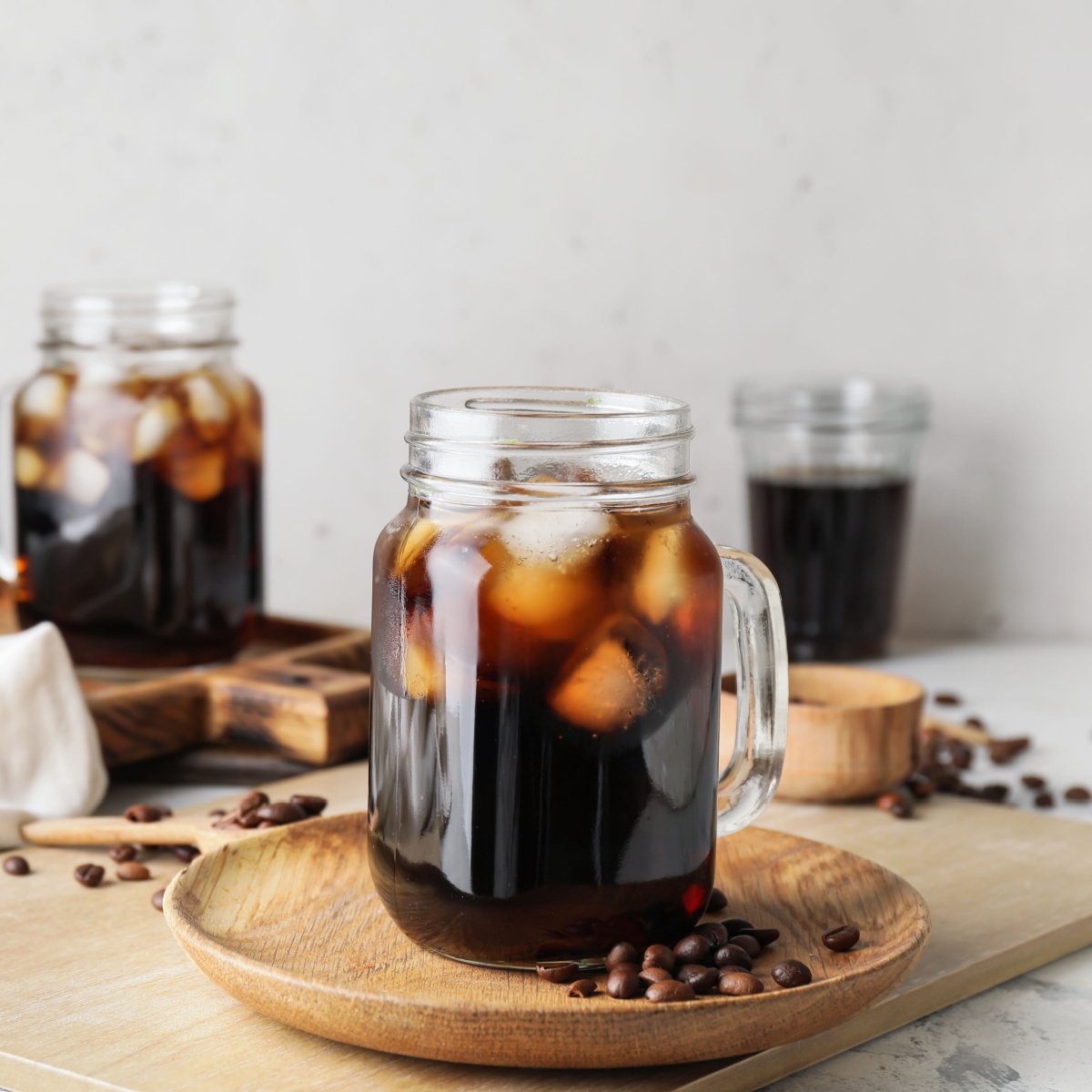 iced cold brew coffee in glass mason jar on wooden saucer with whole coffee beans on wooden tray