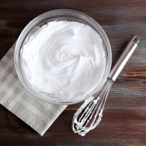 making homemade whipped cream using whisk and big bowl on wooden table