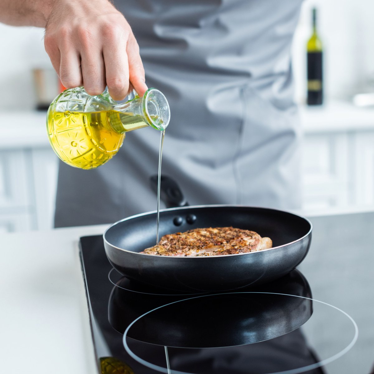 man pouring oil while cooking steak on a pan