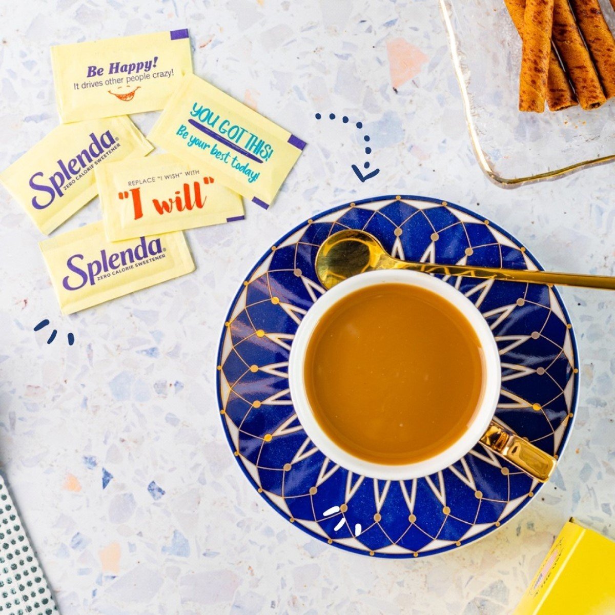 splenda packets beside cup of coffee on blue saucer with gold spoon