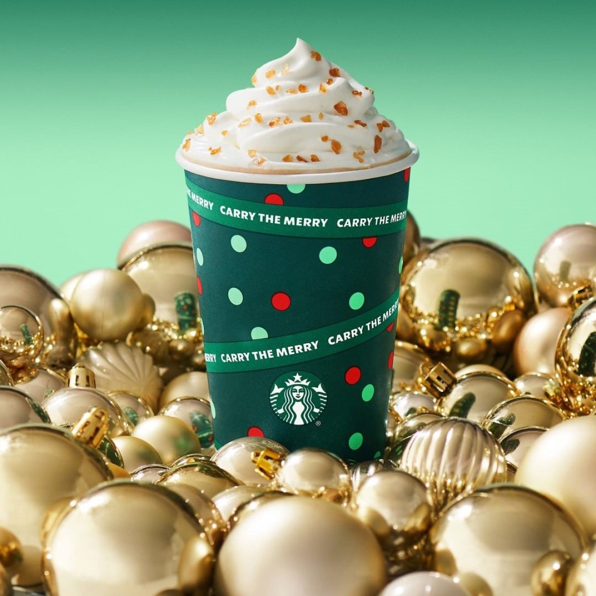 starbucks caramel brulee latte in green christmas paper cup surrounded by golden christmas balls decor