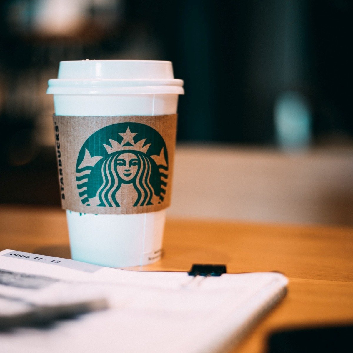 starbucks disposable cup on wooden table beside papers and pen