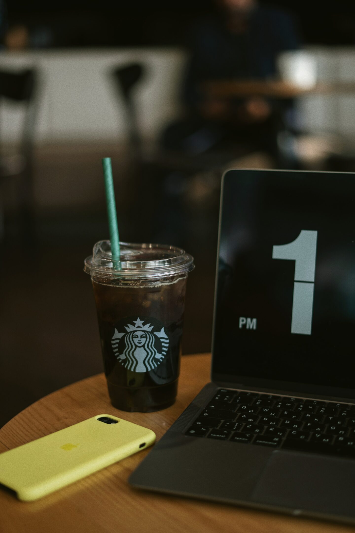 starbucks iced coffee in plastic cup on wooden table beside phone and laptop