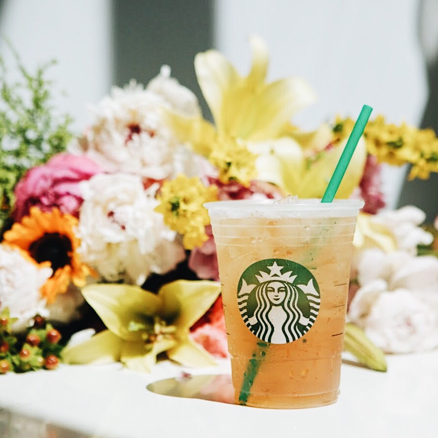 starbucks peach citrus white tea iced shaken tea in plastic cup flowers in background