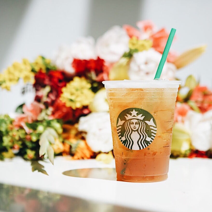 starbucks pineapple black tea iced shaken tea in plastic cup flowers in background