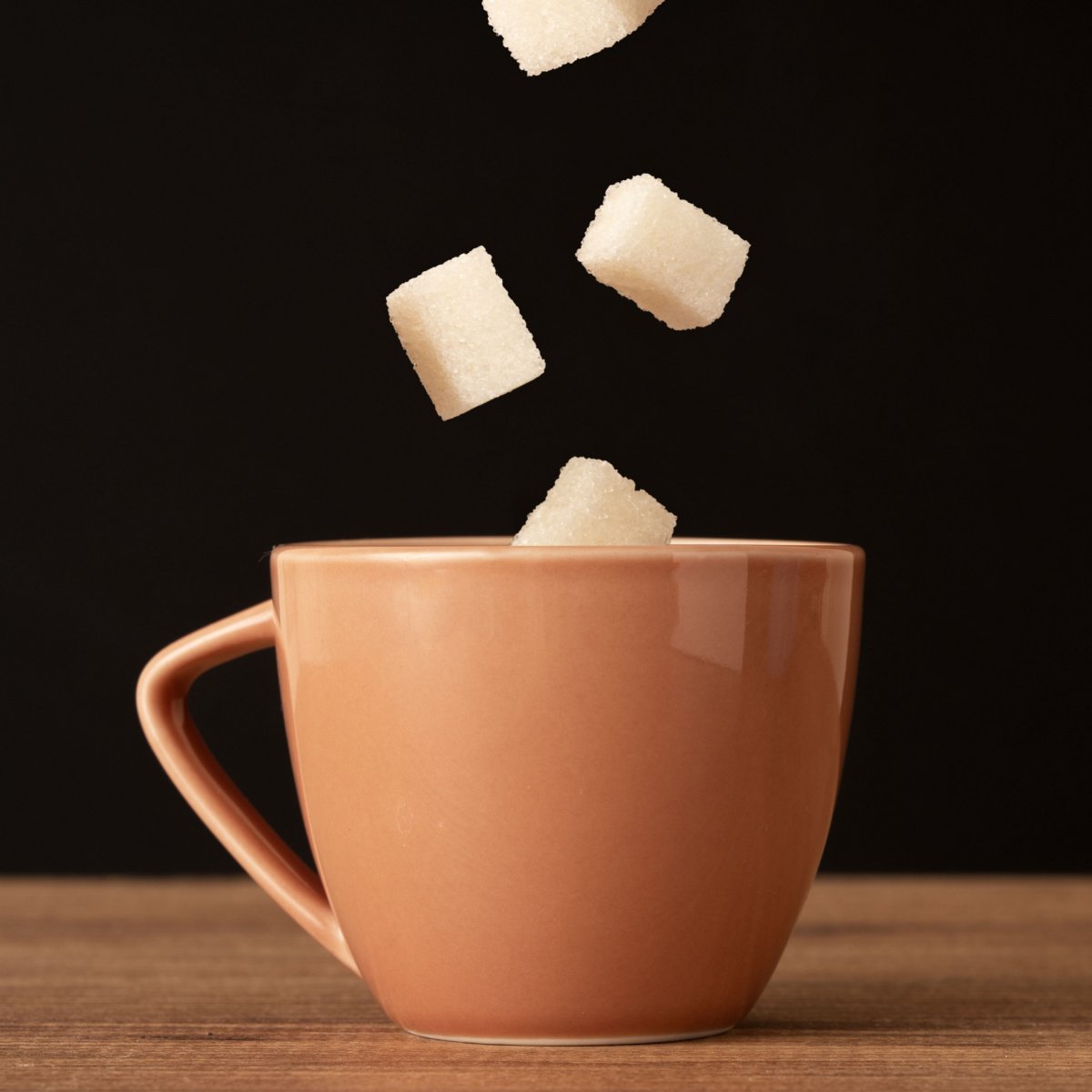 sugar cubes falling=into coffee in ceramic mug on wooden table