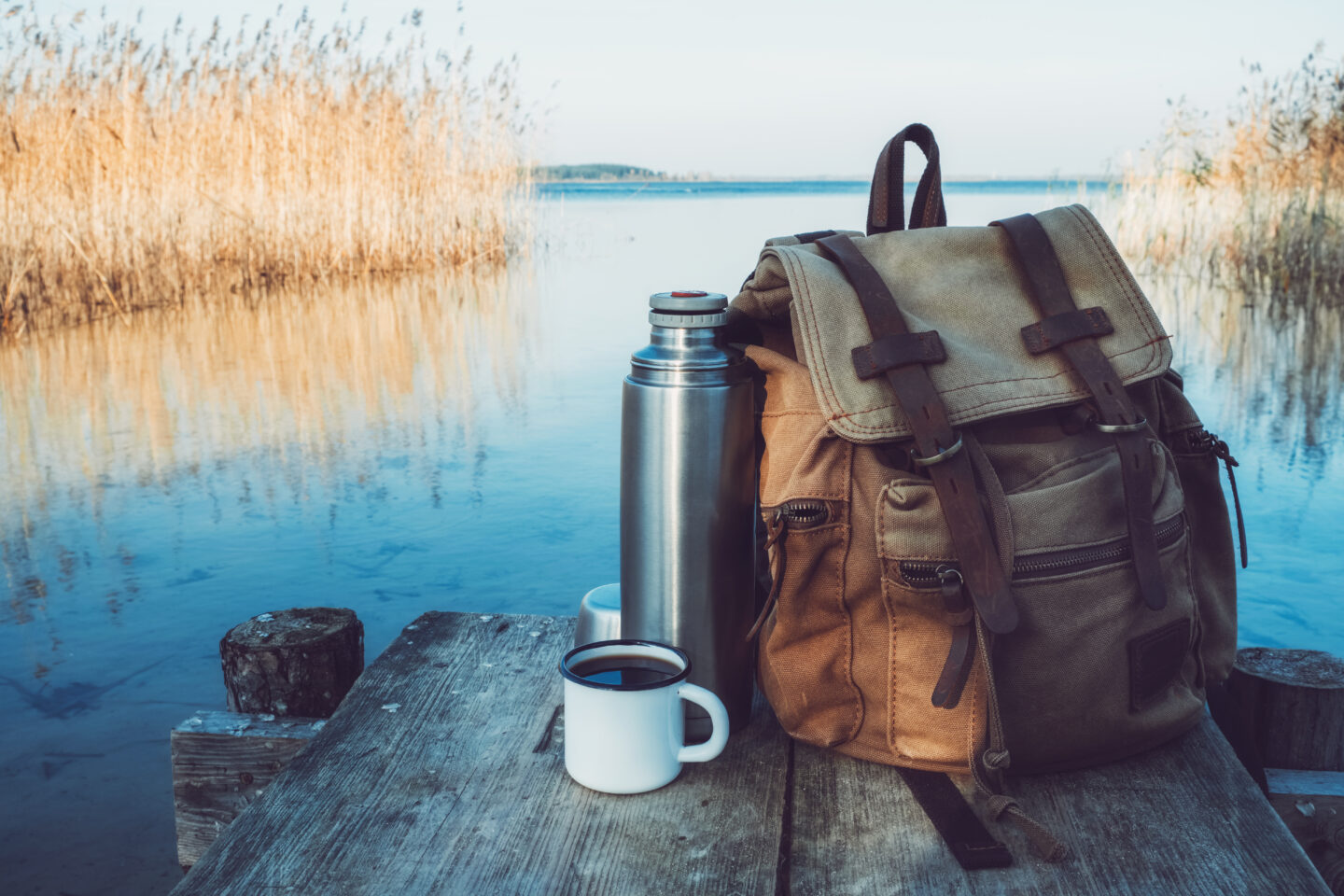 a-mug-and-thermos-with-coffee-beside-a-backpack