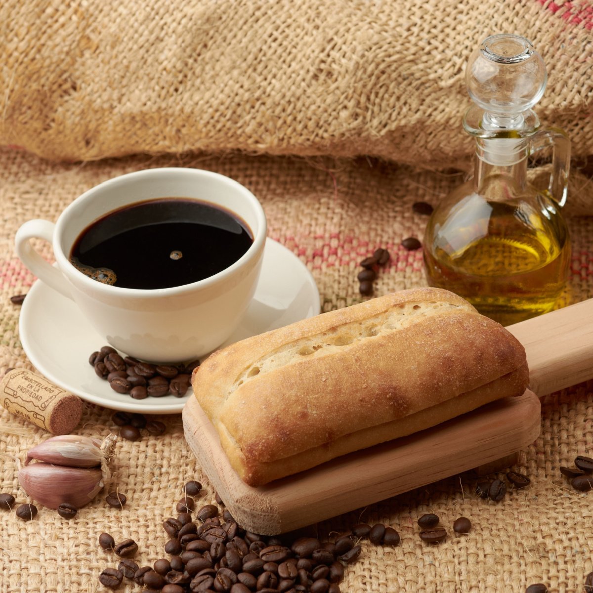 bottle of olive oil beside cup of coffee and bread on sack