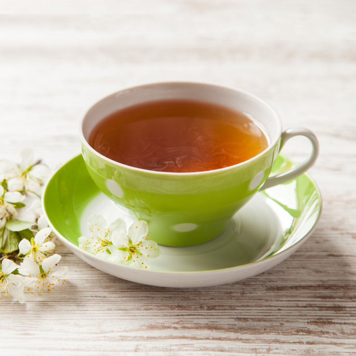 cup of freshly brewed tea in green cup and saucer on wooden table