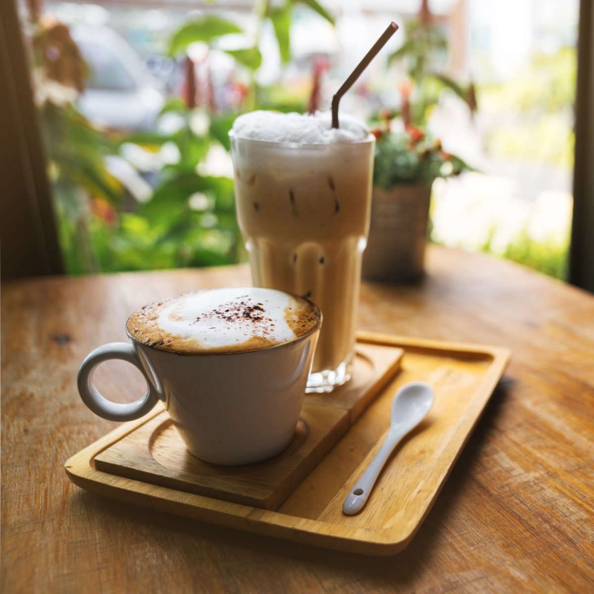 cup of hot latte in ceramic mug beside iced latte on wooden tray