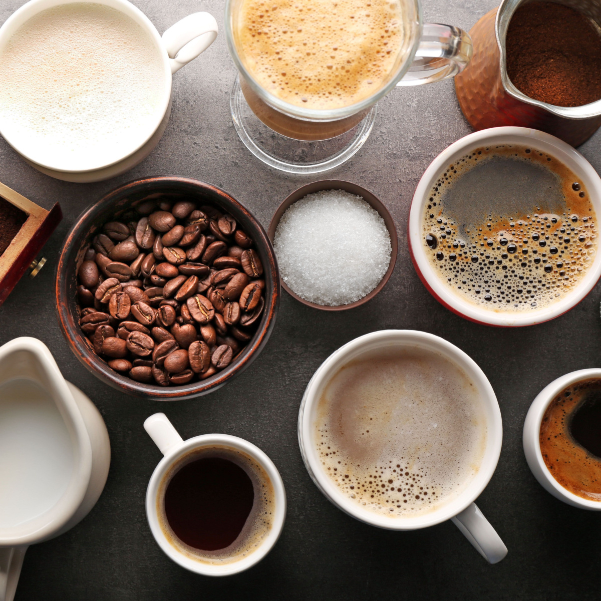 freshly brewed cups of coffee in mugs and glasses beside coffee beans sugar and milk