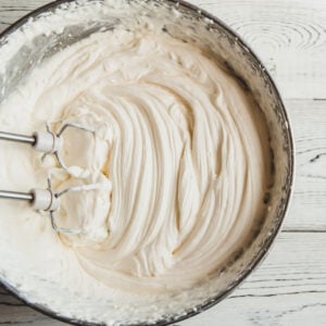 mixer whipping cream into whipped cream in large black mixing bowl on wooden table