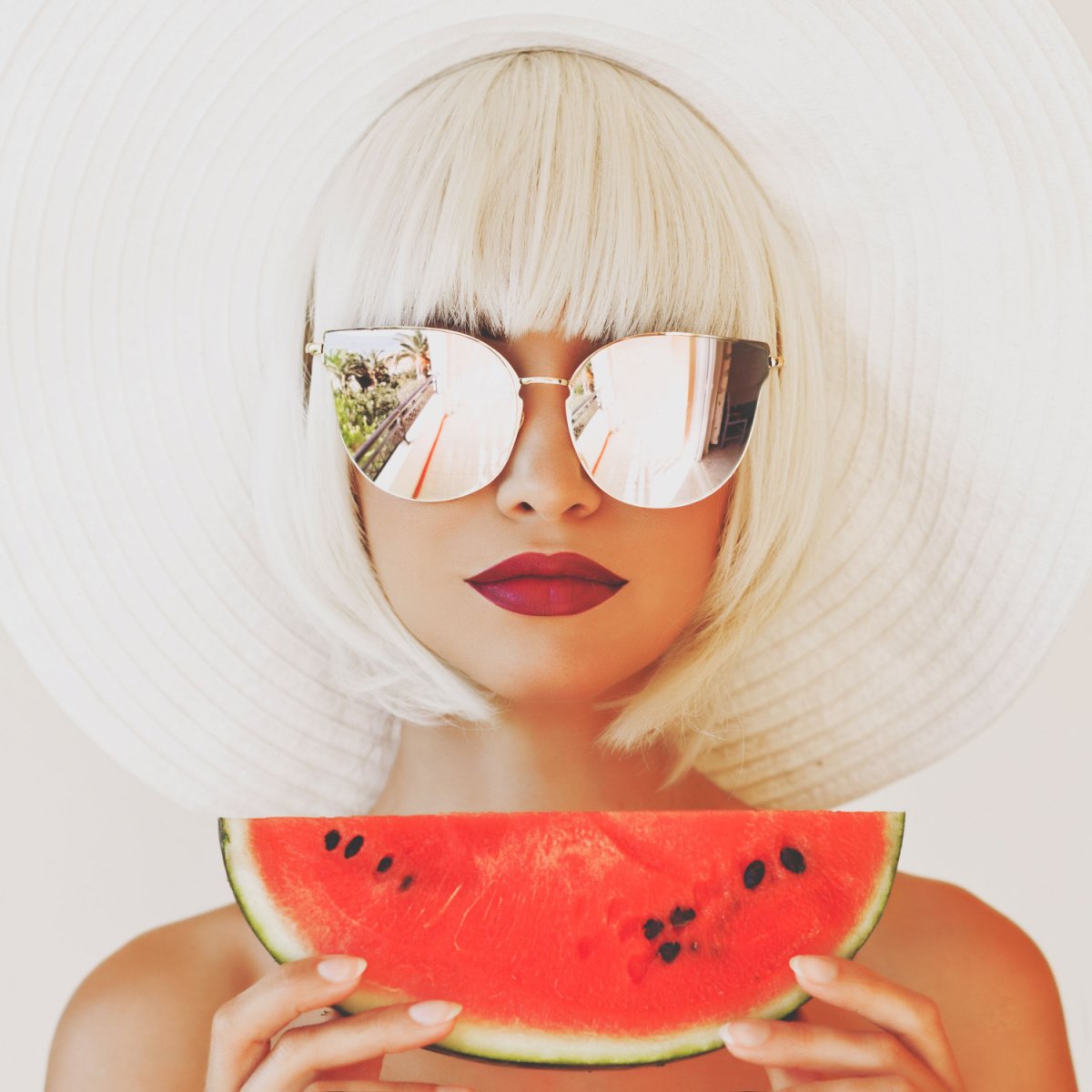 a pretty woman wearing sunglasses and a hat is eating a watermelon slice