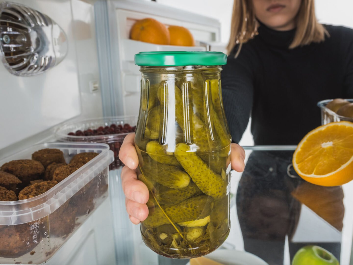 woman places jar of pickles in fridge