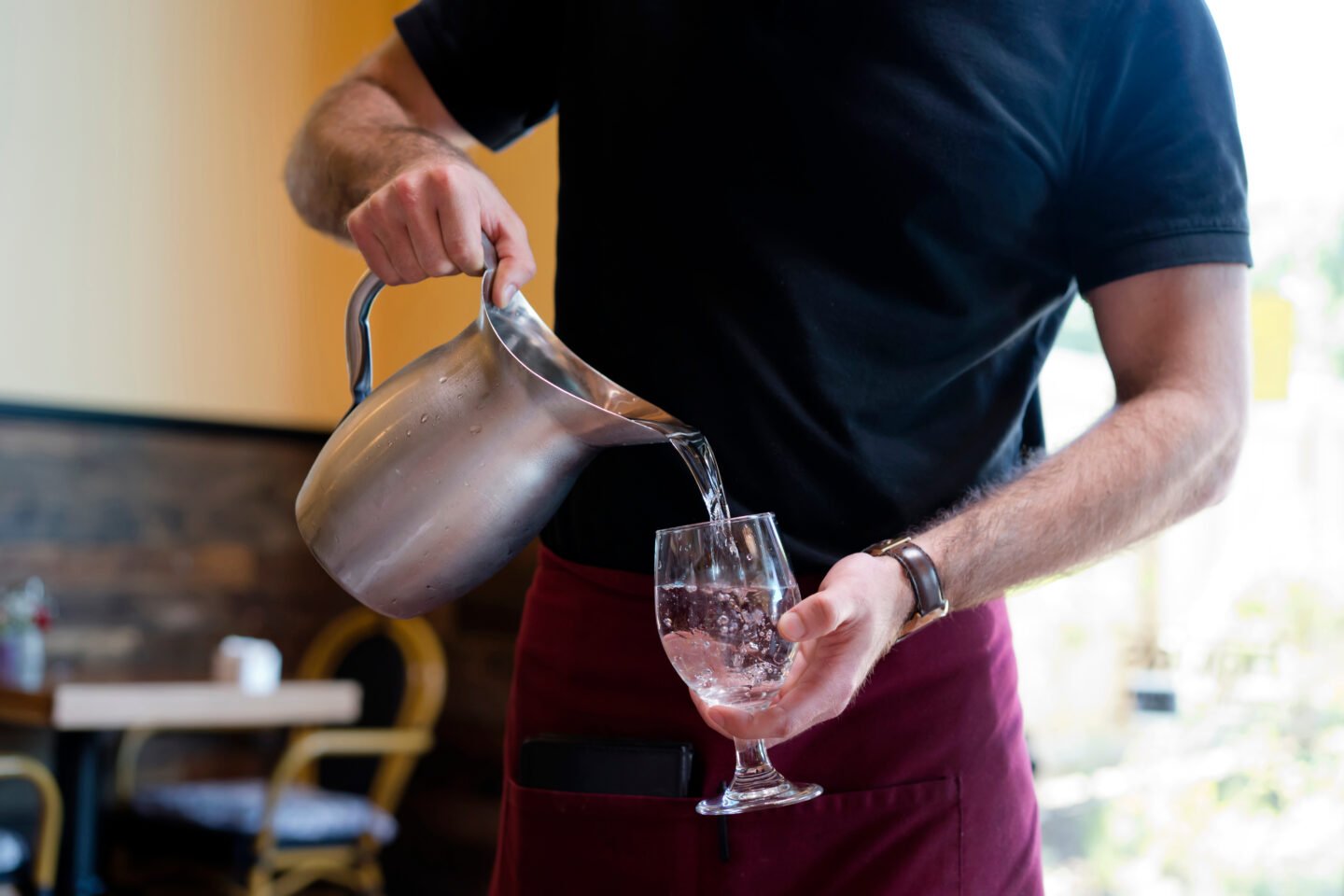 barista-pours-water-from-a-stainless-steel-jug-into-a-customers-glass