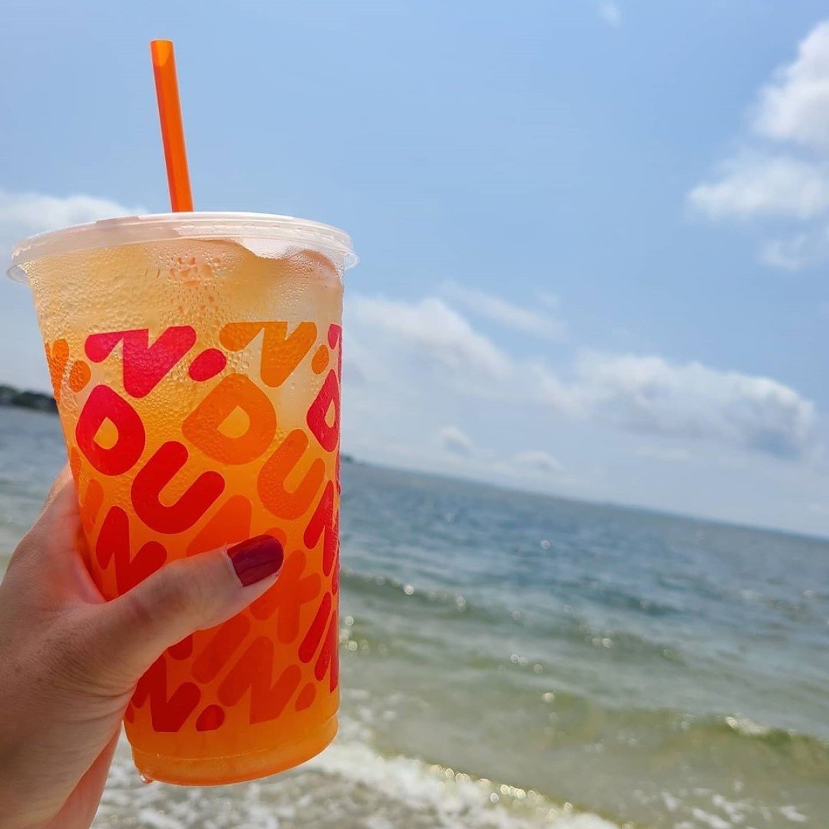 hand holding cup of dunkin refresher at the beach